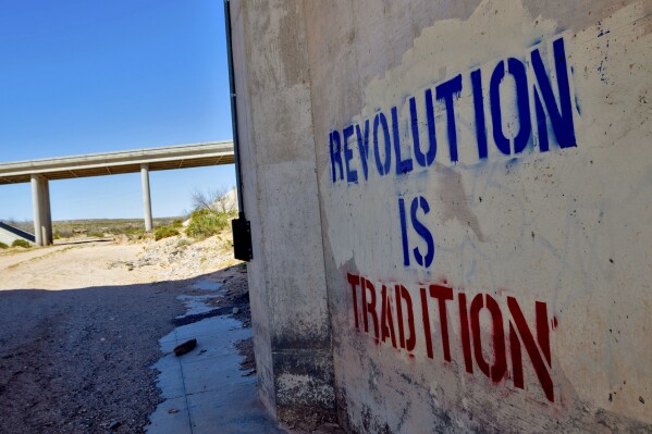 "Revolution is Tradition" appear freshly stenciled on a cement wall, Tuesday, April 9, 2024, in Mesquite, NV beneath a freeway overpass where armed protesters and federal government agents stared each other down through rifle sights 10 years ago. Ten years have passed since hundreds of protesters including armed riflemen answered a family call for help which forced U.S. agents and contract cowboys to abandon an effort to round up family cattle in a dispute over grazing permits and fees. Despite federal prosecutions, no family members were convicted of a crime. (AP Photo/Ty ONeil)